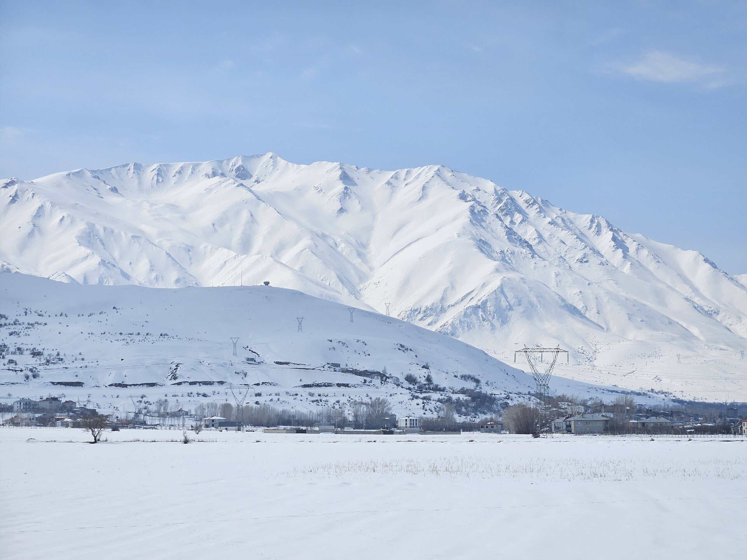 A sweeping mountain panorama during a ski tour in Eastern Anatolia, featuring snow-capped peaks and a traditional village in the valley beneath a blue sky.